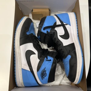 Nike Air Jordan 1 Retro High OG - Snygga Nike Air Jordan 1 Retro High OG i svart, blått och vitt. Använda endast ett par gånger. Perfekt skick. Skorna har en klassisk hög design med snörning och den ikoniska Nike-loggan på sidan. Perfekta för sneakerheads som älskar en stilren look.