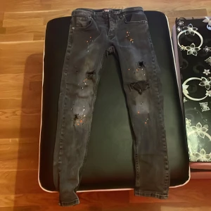 Grå jeans med slitningar från Denim Park - Snygga grå jeans från Denim Park med coola slitningar och färgstänk. De har en slim fit passform och är perfekta för en trendig look. Jeansen har klassisk femficksdesign och knappgylf.