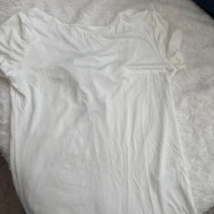 Vit kortärmad topp med rosett - Säljer en söt vit topp med korta ärmar och med knytning i ryggen. Perfekt för en stilren och elegant look. Toppen är gjord i ett mjukt material som känns skönt mot huden. Verkligen så söt!🌸💕🌸💕