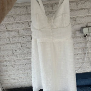 Vit klänning med knytband - Säljer en stilren vit klänning med knytband i ryggen. Klänningen har en texturerad yta och är ärmlös med en vacker passform. Perfekt för sommarens varma dagar eller studenten. Har aldrig kommit till användning så är i nytt skick!💕🌸💕går även att knyta olika i ryggen