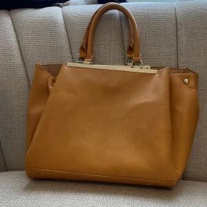 Kamelbrun handväska med metall-detaljer - Säljer en stilren kamelbrun handväska med två handtag och snygga metall-detaljer upptill. Väskan har ett stort huvudfack och innerfack med dragkedja. Perfekt för dig som vill ha plats för allt du behöver i vardagen. Säljer för 85kr vilket är ett superbra pris!🌸 pris går att diskutera.