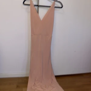 Champagnefärgad långklänning från Bik Bok - Säljer en elegant champagnefärgad långklänning från Bik Bok med djup v-ringning och smala axelband. Klänningen har en figurnära passform och är tillverkad i ett mjukt, slätt material som ger en lyxig känsla.