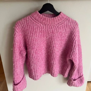 Rosa stickad tröja med grov struktur - Mysig rosa stickad tröja med grov ribbad struktur och rund halsringning. Tröjan har långa ärmar och en avslappnad passform, perfekt för kyliga dagar. Enkel att styla till både jeans och kjol.