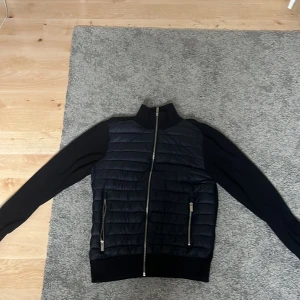 Mörkblå cardigan med dragkedja - Mörkblå cardigan med quiltad front och ärmar i slätare material. Jackan har hel dragkedja framtill och två fickor med dragkedja. Perfekt för dig som vill ha en stilren och sportig look.