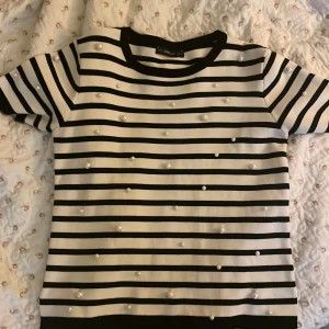 Svartvit randig topp med pärlor - Säljer en svartvit randig topp med korta ärmar och rund hals. Toppen är dekorerad med små pärlor över hela framsidan för en extra detalj. Perfekt för dig som gillar klassiska mönster med en twist. Den kommer ifrån Zara och storleken är M. men den funkar jätte bra om man har xs eller S i storlek.💗