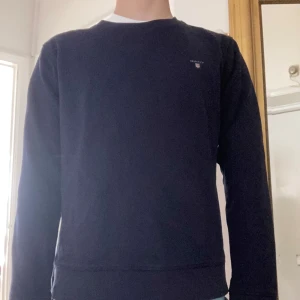 Mörkblå sweatshirt från GANT - Mörkblå sweatshirt från GANT med rund halsringning och diskret broderad logga på bröstet. Klassisk och stilren modell i mjuk bomull, perfekt för en avslappnad look.