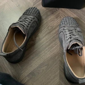 Grå sneakers med nitar - Säljer ett par grå sneakers med snörning och coola nitar på tån. Skorna har rund tå och är tillverkade i mocka. Perfekta för dig som vill sticka ut lite extra med din stil.