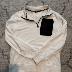 Vit tröja med svart bröstficka från Sail Racing - Säljer en vit långärmad tröja från Sail Racing med svart dragkedja och en stor svart bröstficka med dragkedja. Lite liten i storlek så passar m också. 