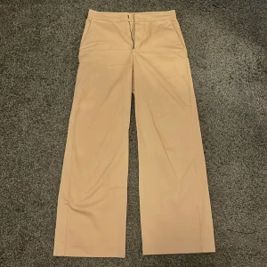 Lindex beiga kostymbyxor med vida ben - Snygga beiga kostymbyxor med hög midja och vida ben från Lindex. Byxorna har klassisk passform med dragkedja och knapp framtill. Perfekta att styla med en enkel topp eller skjorta💛☀️👖