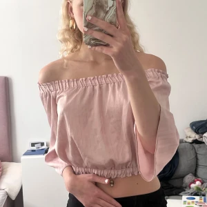 Ljusrosa offshoulder blus - Säljer en ljusrosa offshoulder blus med trekvartsärmar och resår i både överkant och nederkant. Blusen har en luftig passform och är tillverkad i ett mjukt, vävt material. Perfekt för vår och sommar!