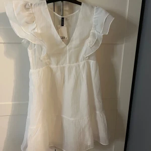  volangklänning  - Superfin vit klänning från H&M med v-ringning och volangdetaljer vid ärmarna. Klänningen har en luftig passform. Aldrig använd och helt ny.