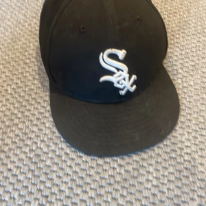 Svart keps från New Era 59FIFTY med White Sox-logga - Säljer en svart keps från New Era 59FIFTY med broderad vit White Sox-logga framtill. Kepsen har böjd skärm och MLB-logga baktill. Klassisk modell i bomull, perfekt för sportiga outfits.