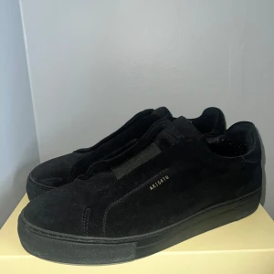 Svarta sneakers från Axel Arigato i mocka - Säljer ett par svarta sneakers från Axel Arigato i mjuk mocka. Skorna har minimalistisk design med diskret guldfärgad logga på sidan och platt sula. Perfekta för dig som gillar stilrena och snygga skor.