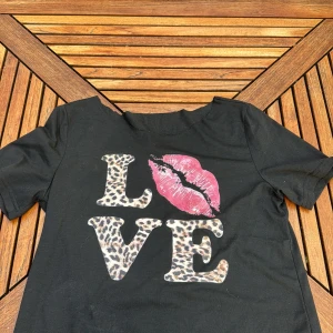 Svart t-shirt med leopardmönster och läppar - Cool svart t-shirt med texten 'LOVE' där bokstäverna är i leopardmönster och ett stort rosa läppavtryck. Perfekt statement-plagg💕skrive om du har frågor 🥰