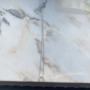 Silverhalsband med cirkelformad hängsmycke - Säljer ett elegant halsband i silver med en tunn kedja och ett cirkelformat hängsmycke dekorerat med gnistrande stenar. Perfekt för dig som gillar stilrena smycken med lite extra bling.