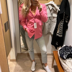 Rosa kavaj från MQ - Snygg rosa kavaj från MQ med klassisk krage och knäppning framtill. Kavajen har fickor med lock och en figurnära passform som ger en stilren look. Perfekt att styla både till jeans och klänning för en trendig outfit.
