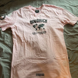 Ljusrosa t-shirt från Hoodrich - Säljer en ljusrosa t-shirt från Hoodrich med svart tryck framtill och coolt världskarta-motiv. T-shirten har rund halsringning och korta ärmar. Perfekt för dig som gillar streetwear och vill sticka ut med en snygg färg.
