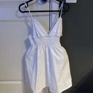 Vit kort klänning med smock från Sister - Söt vit kortklänning från Sister med smala axelband och smockad överdel. Klänningen har en luftig passform och är perfekt för varma dagar. Tillverkad i bomull för en skön känsla.