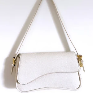Vit axelväska med gulddetaljer - En stilren och klassisk vit handväska som aldrig går ur tiden! Perfekt när man bara behöver ha med sig det nödvändiga men även något extra som kräver plats. 