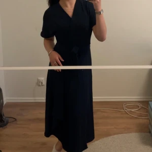 Marinblå klänning - Marinblå lång klänning. Den är omlott, o sätts fast med två knappar (se bild 3). Band bakom ryggen är fastsydda som du kan knyta runt midjan. Väldigt skönt material, och väldigt fin. Använd fåtal gånger, och vill att den kommer till bättre användning