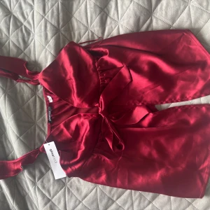 Vinröd omlottklänning i satin - Säljer en vinröd omlottklänning i glansigt satinmaterial från Gina Tricot. Klänningen har smala axelband, knyt i midjan och en feminin v-ringning. Perfekt för dig som vill sticka ut med en elegant look.Köpt för 299 och aldrig avänd