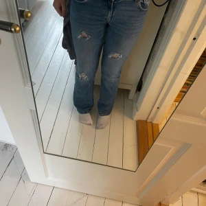 Blå slitna jeans från Gina Tricot - Säljer ett par blå jeans från Gina Tricot med slitningar på knäna och låren. Byxorna är utsvängda, normal passform och dubbla knappar i midjan. Klassisk femficksmodell och tillverkade i denim💕