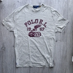 Polo Ralph Lauren T-Shirt - Grey Melange - *Slutsåld i affär, tillverkas ej längre!* Gråmelerad T-Shirt från Polo Ralph Lauren med vinrött tryck på framsidan i nästan nytt skick. Använd 1-2 gånger. Storlek: Medium, passar M-L. Tveka inte, hör av er vid funderingar! 😄