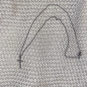 Silverhalsband med glittrigt kors - Ett stilrent halsband i silverfärg med ett korshänge täckt av små glittrande stenar. Kedjan är tunn och har ett klassiskt lås. Perfekt för dig som gillar enkla men snygga smycken med lite extra bling. Använd ett par gånger bara.