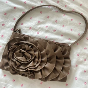 Brun axelväska med stor rosett -  brun axelväska i skinnimitation med en stor rosettdetalj framtill. 