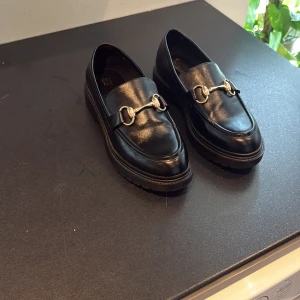 Platåloafers i skinn med guld spänne från Din Sko - Hej! Säljer ett par Din Sko platåloafters som knappt är använda, har haft dem ett tag men syns inte. Dem är i storlek 39.
