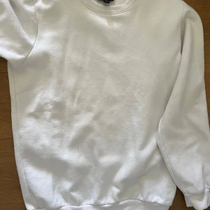 Vit sweatshirt från SMOG - Klassisk vit sweatshirt från SMOG i regular fit. Tröjan har rund halsringning och ribbade muddar vid ärmslut och nederkant. Perfekt basplagg för garderoben.