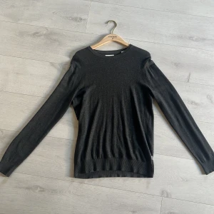 Svart/mörkgrå tunn stickad tröja - En stilren svart tunn stickad tröja med rund halsringning och långa ärmar. Tröjan har en enkel design utan synliga detaljer. Använt max 1-2 gånger helt ny från jack and jones.
