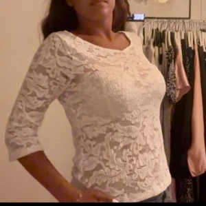 Vit spetsblus med trekvartsärm - Säljer en vit blus i spets med blommigt mönster och trekvartsärmar. Blusen har rund halsringning och är lätt transparent, vilket ger en snygg och feminin look. Perfekt att styla med jeans eller kjol för en trendig outfit.