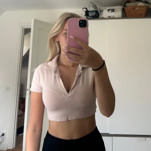 Ljusrosa croppad polotopp - Säljer en ljusrosa croppad polotopp med krage och v-ringning. Toppen har korta ärmar och är perfekt för en trendig och avslappnad stil. Från H&M storlek S