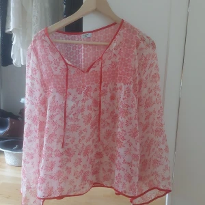  Världens sötaste blusen från b.young - Säljer en luftig och transparent blus från b.young i vitt med röda blommor. Blusen har v-ringning med knytband och långa ärmar. Perfekt för varmare dagar när du vill ha något lätt och snyggt. 💞💞