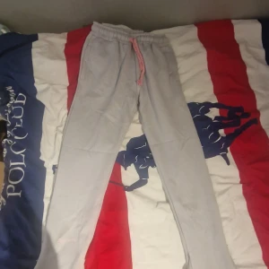 Ljusgrå mjukisbyxor från syna world - Ljusgrå mjukisbyxor från syna world med resår och dragsko i midjan samt tryckt logga baktill. Byxorna har en relaxed passform och är perfekta för en avslappnad stil.