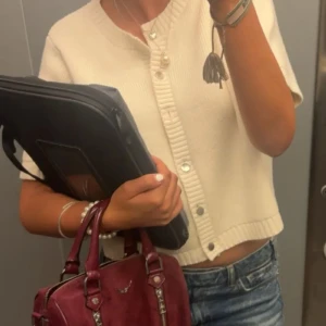 Vit stickad kofta med kort ärm från Gina Tricot - Säljer en söt, croppad vit stickad kofta med silvriga knappar från Gina Tricot. Koftan har korta ärmar, rund halsringning och knappar framtill och är lätt ribbad .  Också superfin att ha uppknäppt som en bolero över en klänning i sommar.