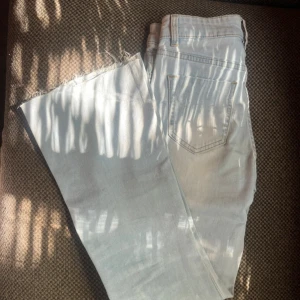 Ljusblå bootcut jeans med rå kant - Säljer ett par ljusblå jeans med bootcut-modell och rå, avklippt kant nertill. Klassisk femficksdesign och bälteshällor. Jeansen har en snygg, ljus tvätt och är perfekta för dig som gillar en avslappnad men trendig look.