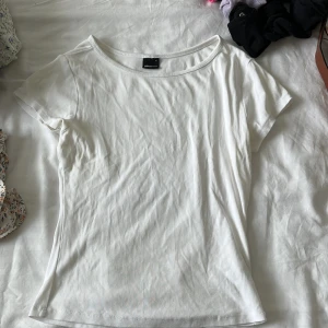 Vit kortärmad topp från Gina Tricot - Enkel och stilren vit topp från Gina Tricot i mjuk bomull. Modellen har rund halsringning och korta ärmar, perfekt att matcha med jeans eller kjol. Klassisk passform som funkar till många olika looks.