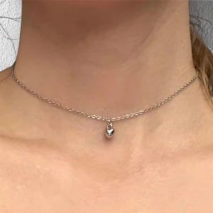 Hjärta silver imitation choker  - Ett litet silvrigt hjärta trätt på en kortare kedja i silverimitation. Justerbar 35-40 cm. För en stilren och samtidigt gullig look!    