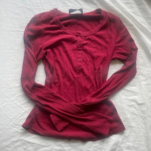 Röd långärmad topp!! - Säljer en röd långärmad topp med knappar framtill. Tröjan har en figurnära passform som framhäver siluetten. Perfekt att styla med jeans eller kjol för en snygg look. Köp nu går bra eller skriv om du har frågor!🫶🏻