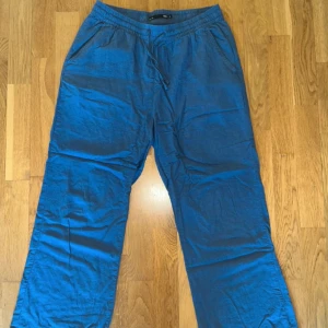 Blå linnebyxor från lager 157 - Säljer ett par blå linnebyxor från lager 157 i storlek S. Byxorna har resår i midjan, snörning och sidofickor samt en bakficka. De har en avslappnad passform och raka ben, perfekta för varmare dagar.