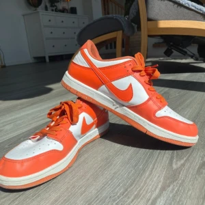 Nike SB Dunk Low Pro Orange/White - Säljer ett par Nike SB Dunk Low Pro i orange och vitt. Skorna har klassisk låg siluett, vit bas med orange overlays och matchande orange snörning. Perfekta för dig som gillar streetwear och skate. Snygg och sportig look med bekväm passform.