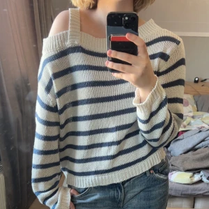 Randig offshoulder stickad tröja - Säljer en stickad offshoulder tröja med breda blå och vita ränder. Tröjan har lång ärm och en croppad passform. Perfekt för dig som gillar en avslappnad men trendig stil.