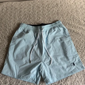 Polo Ralph Lauren Ljusblå Badshorts - Säljer ett par ljusblå badshorts från Polo Ralph Lauren, använd bara en gång vid test. Storlek L, om du använder storlek M passar den perfekt för dig om du vill ha till knän på dem.