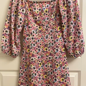 Blommig kortklänning från H&M Divided - Superfin kortklänning med blommigt mönster i rosa, gul, vit, blå och svart. Klänningen har puffiga långärmar och smockad överdel. Perfekt för sommarens alla tillfällen och ger en färgglad vibe. Materialet känns lätt och bekvämt. i slutet av armen finns det resår även på ryggen