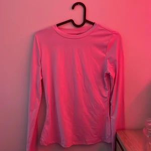 Ljusrosa långärmad tröja - Enkel och stilren ljusrosa långärmad tröja med rund halsringning. Tröjan är slät utan mönster eller detaljer och har en mjuk, lätt stretchig känsla. Perfekt att matcha med jeans eller kjol för en clean look.