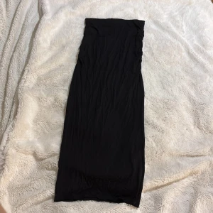 Svart långkjol från Gina Tricot - Snygg svart långkjol med små ”räffel” detaljer på sidorna av höften. Kjolen har en enkel design med en tight passform som framhäver figuren. Kjolen har ett tjockt resår band så den sitter där den sitter 