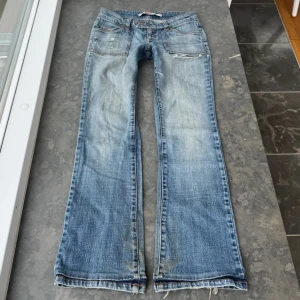 Blå bootcut jeans med slitningar - Snygga blå bootcut jeans med slitna detaljer och råa kanter nertill. Jeansen har klassiska fickor fram och bak, orangea sömmar och en cool, lite tvättad look. Perfekta för dig som gillar en avslappnad och trendig stil. 38cm midjemått tvärs,77cm innerbenslängden 