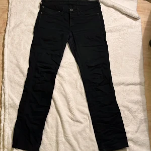 Svarta straight jeans - Svarta jeans från Wrangler med klassisk femficksdesign och raka ben. Byxorna har normal passform och är tillverkade i ett slitstarkt bomullsmaterial med en snygg, stilren look. Perfekta för dig som gillar enkel och tidlös stil.